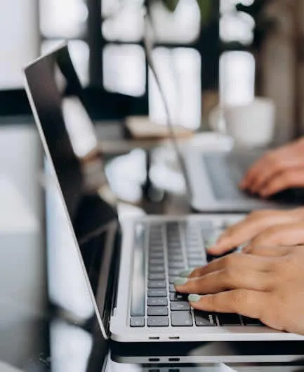 Close-up of hands typing on a sleek laptop keyboard in a bright, modern office setting.