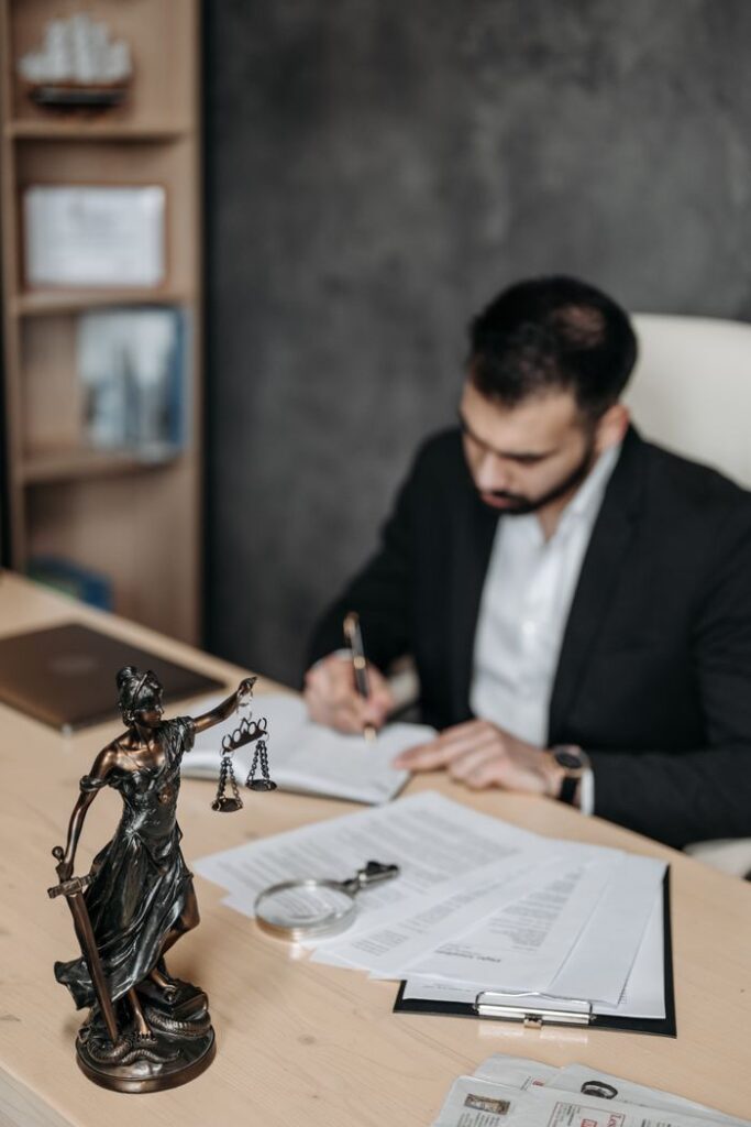 pexels-photo-8112126-8112126 A lawyer concentrates on paperwork in an office; legal statue visible on desk.