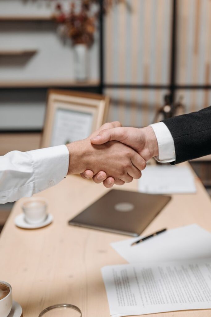 Umowy i transakcje gospodarcze Close-up of two people shaking hands in an office, symbolizing agreement and partnership.